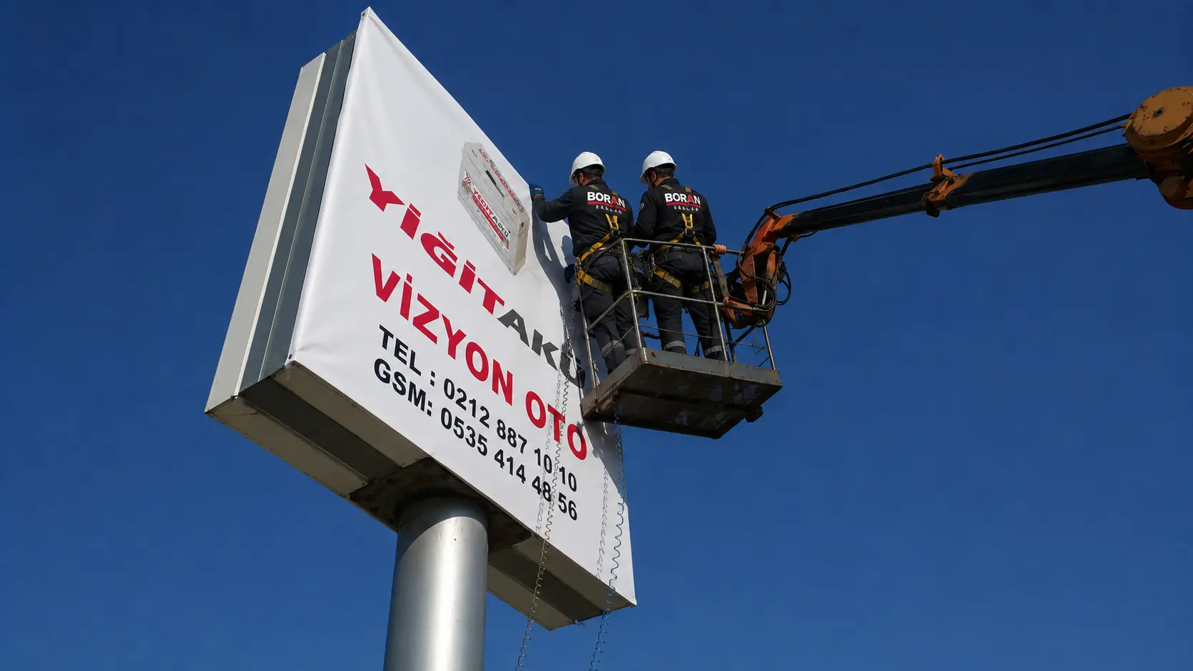 Boran Reklam installers working on the Yiğit Akü pylon sign from an elevated platform