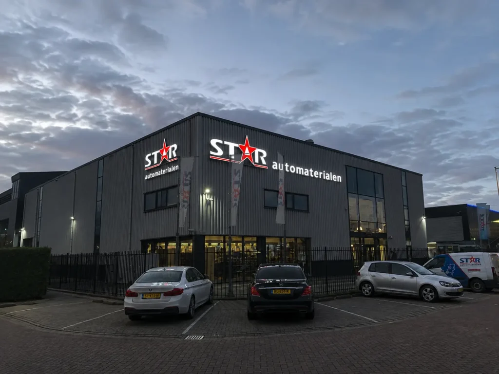 Two illuminated STAR automaterialen signs on the building at dusk