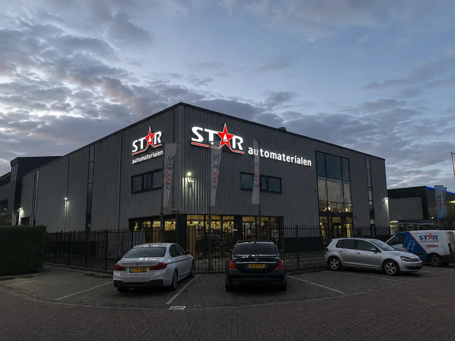 Two illuminated STAR Automaterialen signs visible on adjoining building facades at dusk